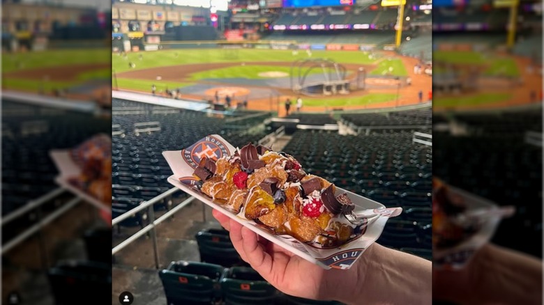 Hand holding a white tray with solid horchata balls, strawberries, plantains, chocolate, and drizzled cream