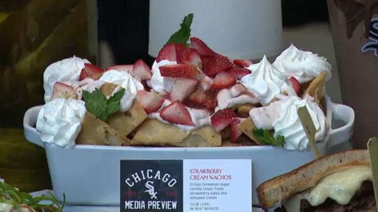 Cinnamon sugar tortilla chips, whipped cream, chopped strawberry, and mint sprigs in a white pan behind a card from a White Sox media preview