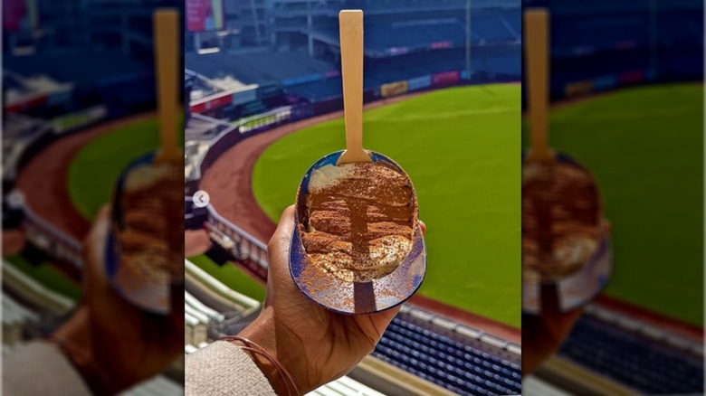 Hand holding souvenir plastic baseball helmet that has tiramisu inside with a disposable spoon