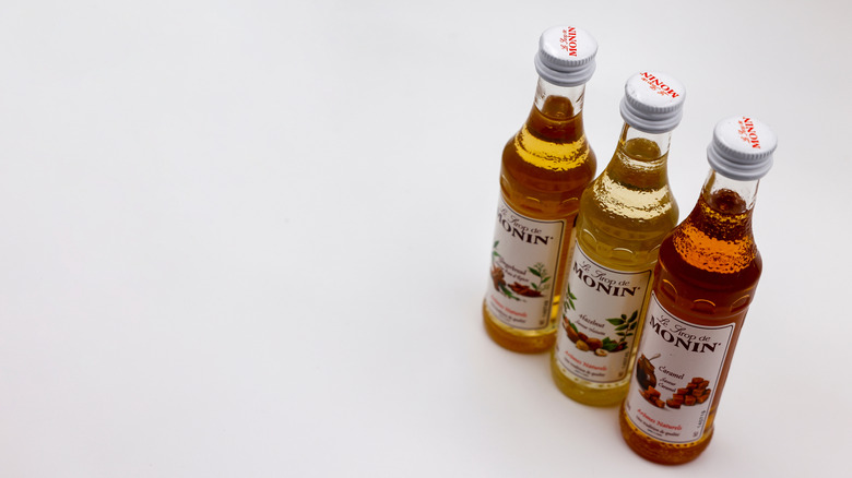 three bottles of Monin syrups, Caramel, Hazelnut, and Gingerbread, on white surface