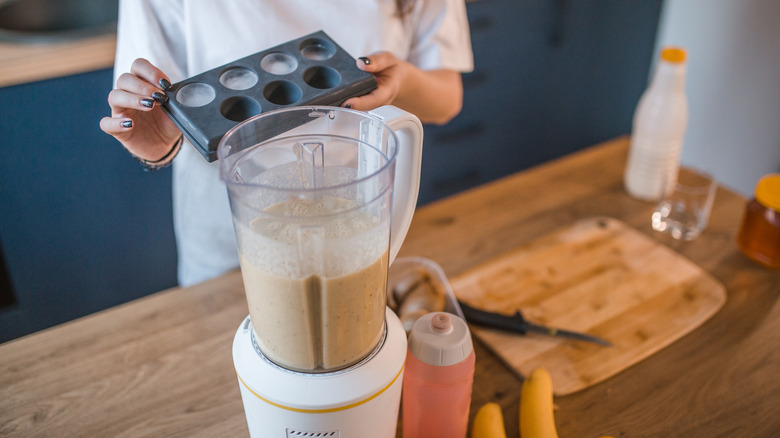 woman adding ice cubes to smoothie in blender