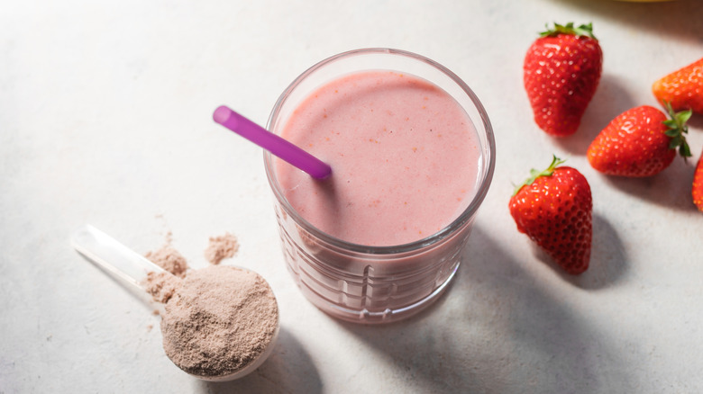 strawberry protein powder sits beside smoothie and fresh strawberries