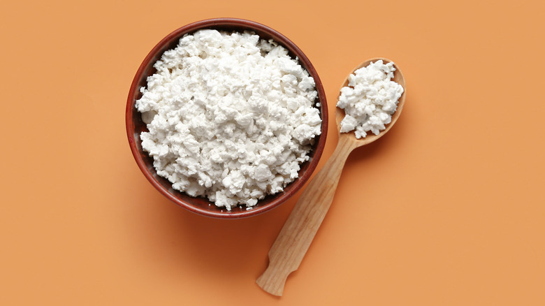 spoon and bowlful of cottage cheese against bright orange background