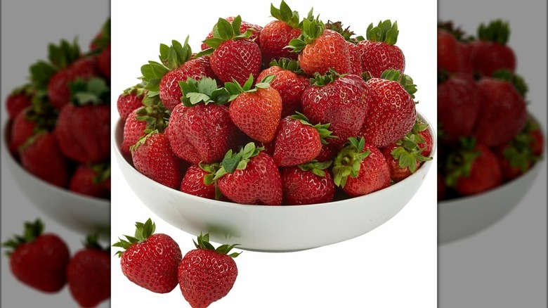 A white bowl full of whole strawberries on a white background