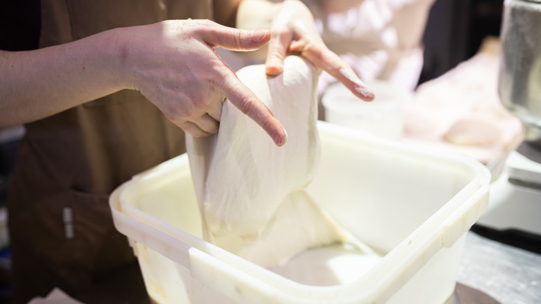 Hands folding dough in  large container