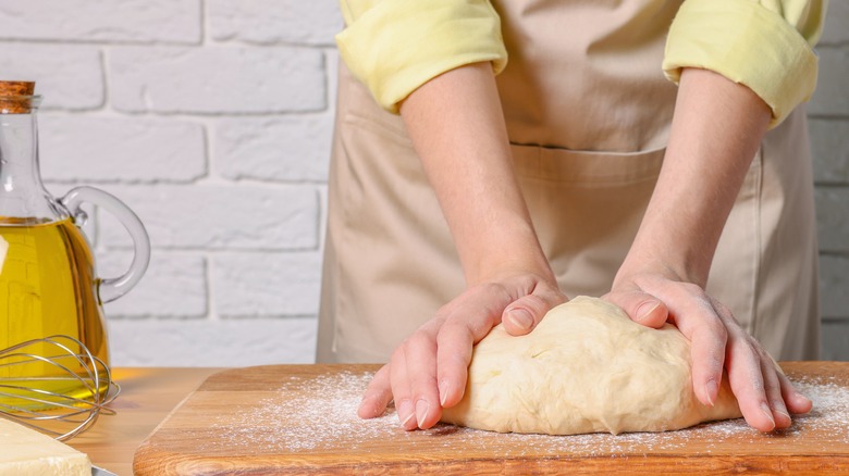 Woman kneading dough on board with jar of oil nearby