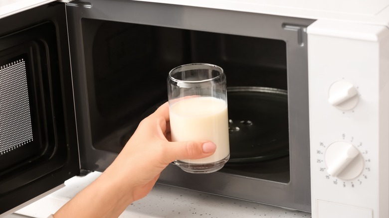 Woman's hand putting glass of milk into microwave