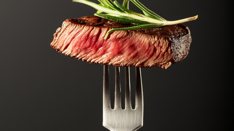 A hunk of steak speared on fork with rosemary