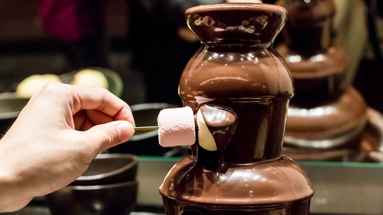 hand dipping colorful marshmallows into chocolate fondue fountain