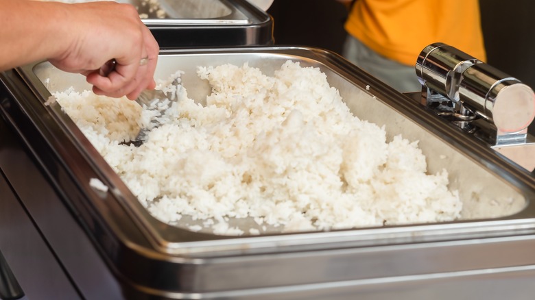 person scooping white rice from metal buffet tray