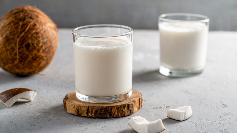 Two glasses of coconut milk with a coconut and pieces of coconut shell