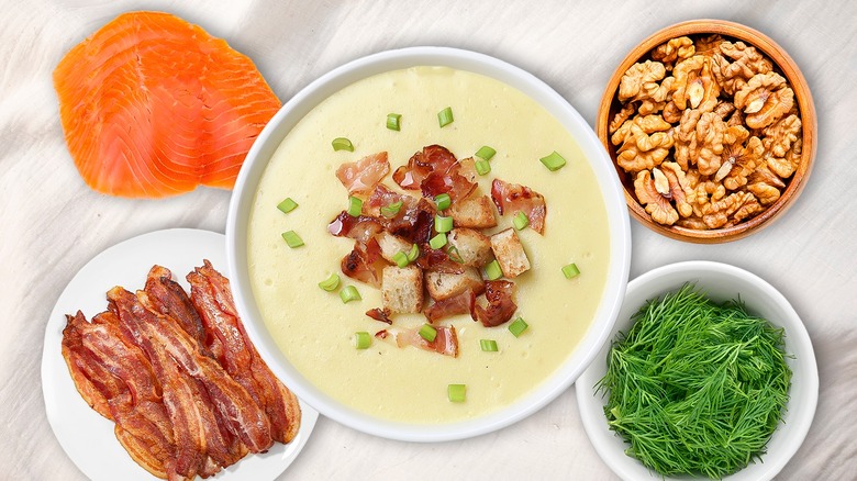 Bowl of potato soup with chives and bacon on top, surrounded by bowls of other ingredients