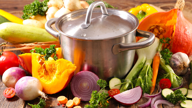 A covered soup pot surrounded by vegetables