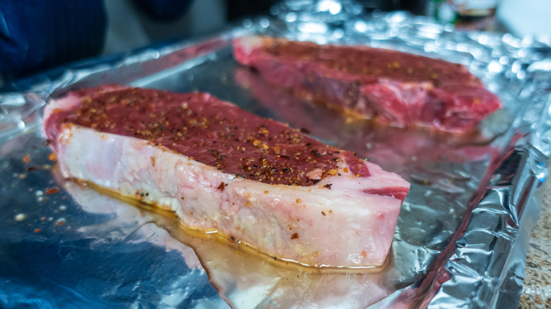 raw steaks on pan lined with aluminum foil