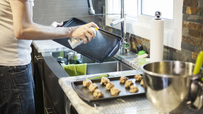 person using cooking spray on baking sheet