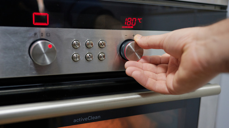 hand preheating an oven by turning dial