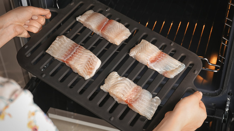 person with painted nails putting broiler pan of fish in oven