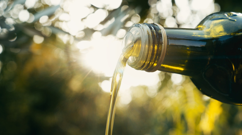 olive oil pouring from bottle with bokeh background