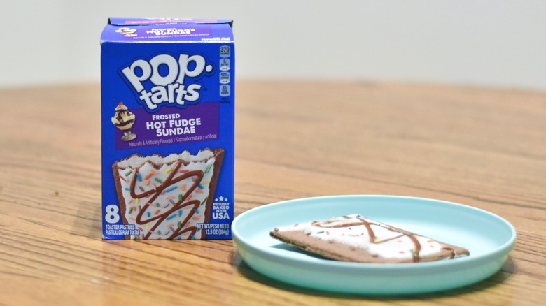 A box of Hot Fudge Sundae Pop Tarts on a wooden table next to a plate