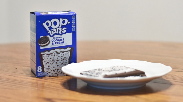 A box of Cookies & Creme Pop Tarts on a wooden table next to a plate