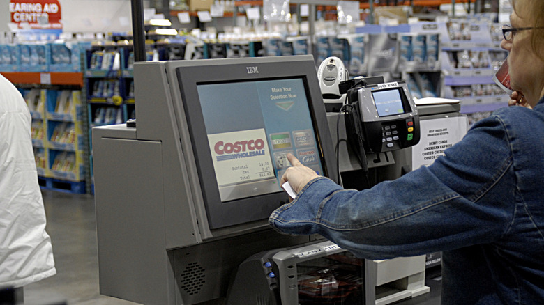 A Costco store employee verifies a membership card at the cash register