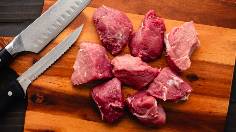 Chunks of pork shoulder on a cutting board beside two knives