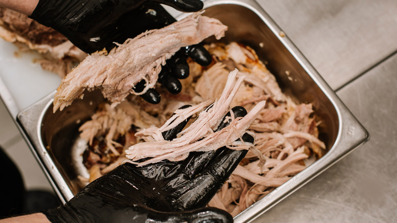 A person holding shredded pulled pork with gloves on