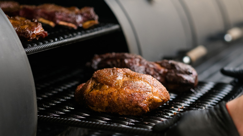 A person pulling pulled pork out of a barbecue smoker