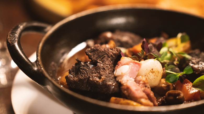 A black bowl with beef bourguignon on a white platter