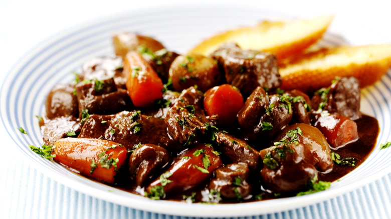 A white bowl of beef bourguignon with crusty bread