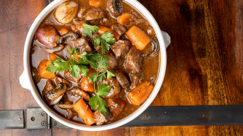 A white bowl of beef bourguignon with herb garnish on a wooden table