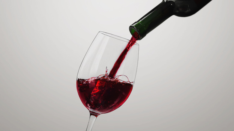 A bottle of red wine pouring into a stemmed wine glass