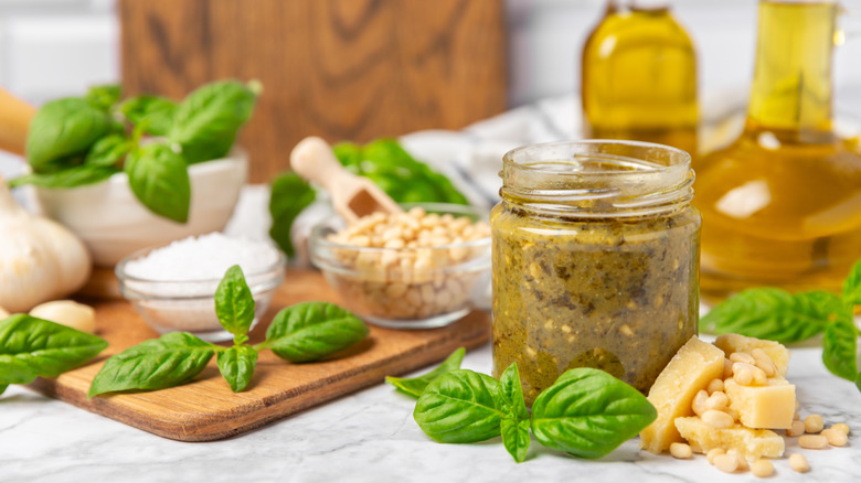 Jar of homemade pesto with ingredients on the board behind