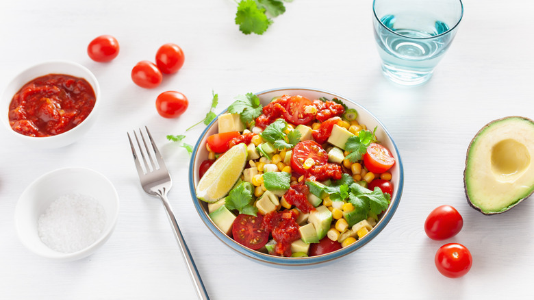 Sweetcorn and tomato salsa on white tablecloth with ingredients surrounding it