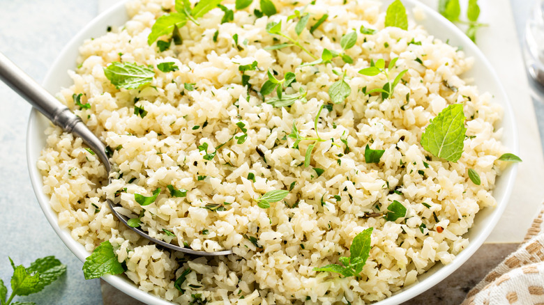 A large bowl of herbed cauliflower rice sits on the counter with a serving spoon.