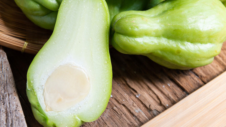 Raw chayote squash are cut in half on a wooden background