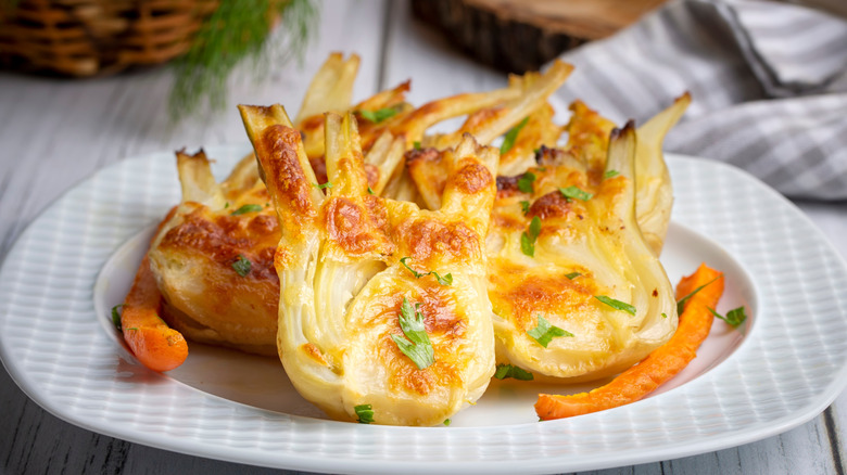 Pieces of roasted fennel on a white plate with carrots on the side