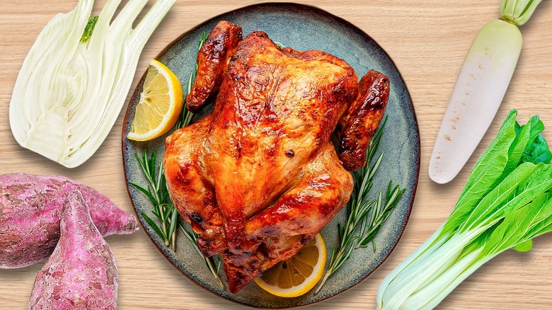 Whole baked chicken on plate surrounded by various vegetables