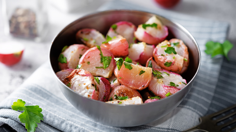 A bowl of roasted radishes with herbs sits on a gray checkered cloth napkin