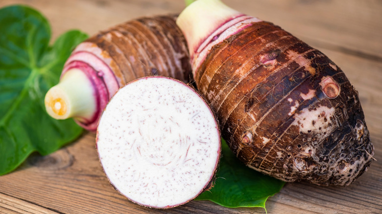 Sliced raw taro roots sit on a wooden table with leaves in background