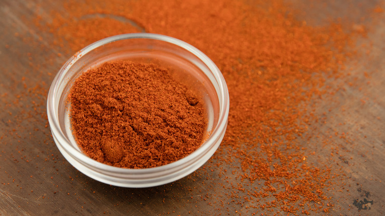 A glass bowl of cayenne pepper on a wooden counter with cayenne pepper sprinkled underneath