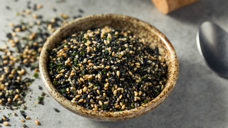 A brown bowl of furikake seasoning with seaweed and sesame seeds on a gray counter