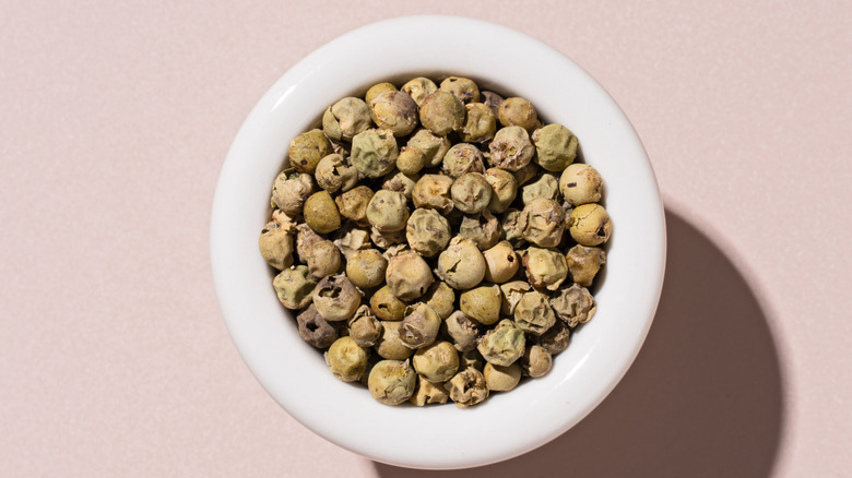 A white bowl with whole green peppercorns on a tan background