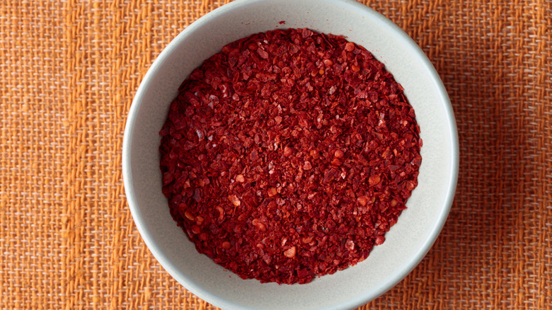 A white bowl of gochugaru red pepper flakes on an orange woven mat