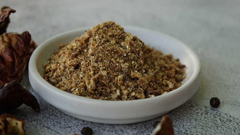 A white bowl of dried porcini mushroom powder on a gray background