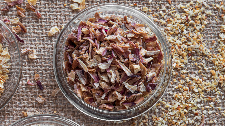 A glass bowl of dried purple shallot flakes on a tan woven mat