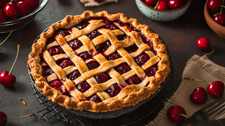 cherry pie with lattice on dark countertop with fresh cherries around it