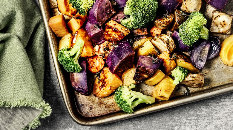 various roasted vegetables on a metal baking sheet next to a green kitchen towel