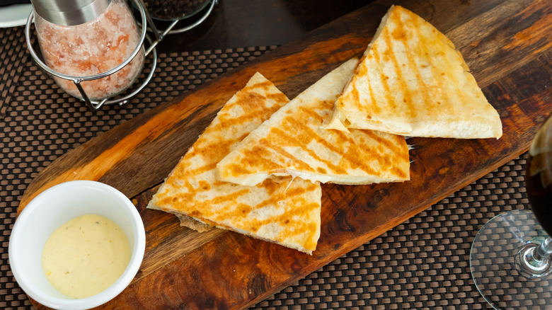 3 cheese quesadillas on a wooden cutting board with sauce