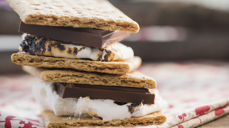 2 s'mores with marshmallow, graham cracker, and chocolate stacked on top of each other on a kitchen towel